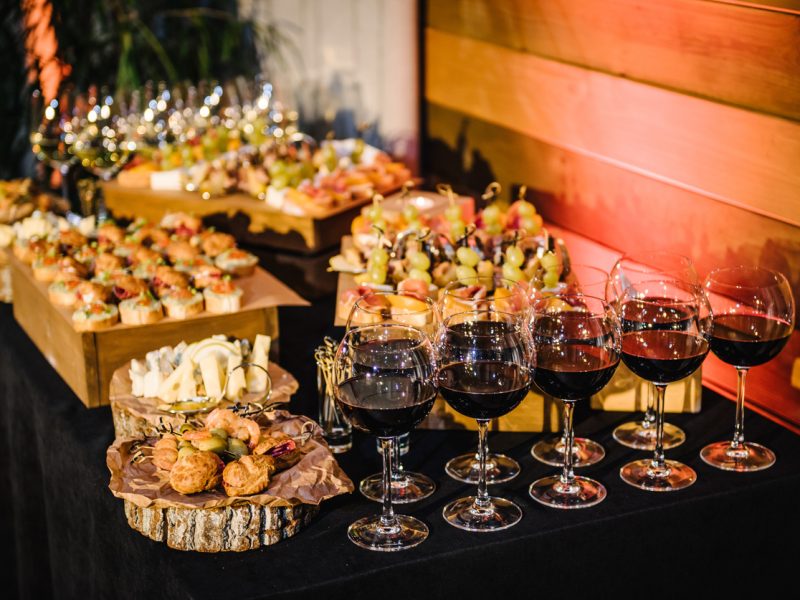 Buffet table. Mini cold snacks, canapes, and appetizers with alcohol for public catering on black table. Food on wooden plates, serving board on festive table, corporate food. Party and holiday away.